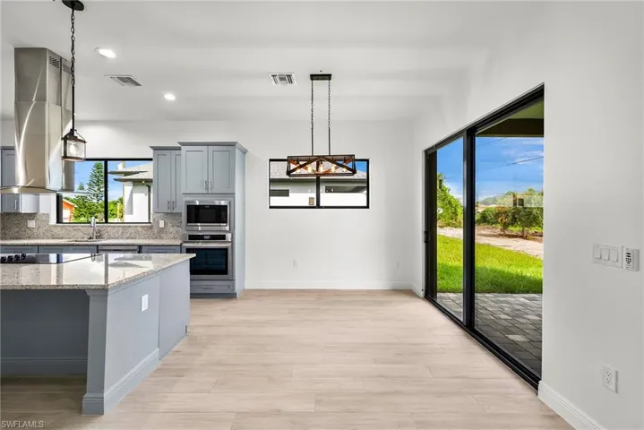 Kitchen featuring hanging light fixtures, backsplash, light stone counters, stainless steel appliances, and light hardwood / wood-style floors