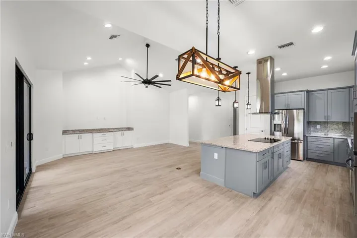 Kitchen with light wood-type flooring, stainless steel fridge, an island with sink, and gray cabinetry