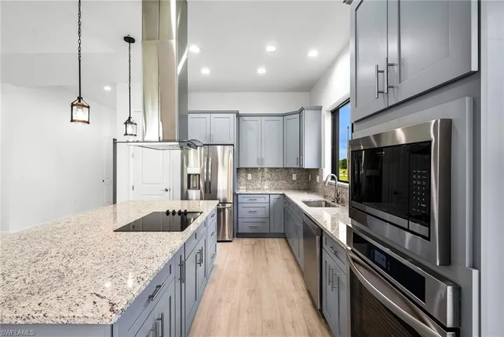 Kitchen featuring light stone countertops, decorative light fixtures, appliances with stainless steel finishes, sink, and gray cabinets