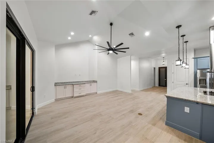 Kitchen with white cabinets, light hardwood / wood-style flooring, light stone counters, lofted ceiling, and ceiling fan