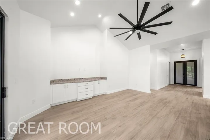 Unfurnished living room with light wood-type flooring, ceiling fan, lofted ceiling, and french doors
