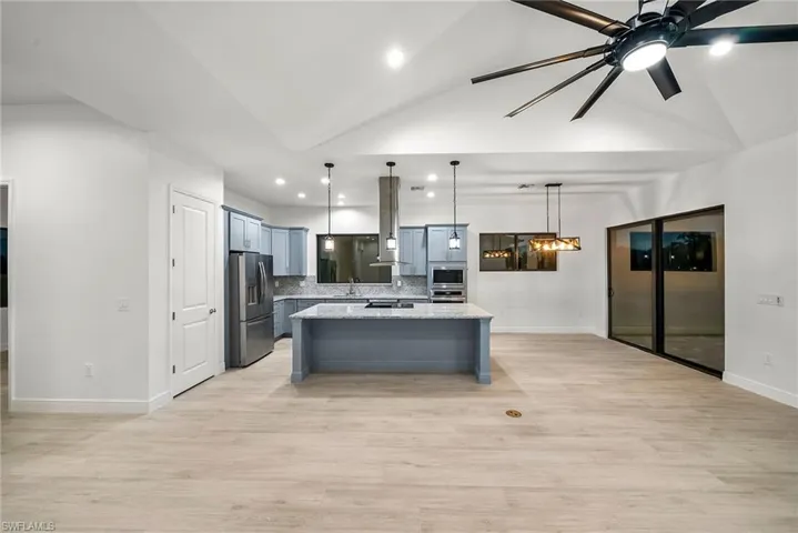 Kitchen with ventilation hood, a center island, decorative light fixtures, light stone countertops, and ceiling fan