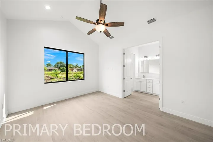 Unfurnished bedroom with ensuite bath, vaulted ceiling, ceiling fan, and light hardwood / wood-style floors