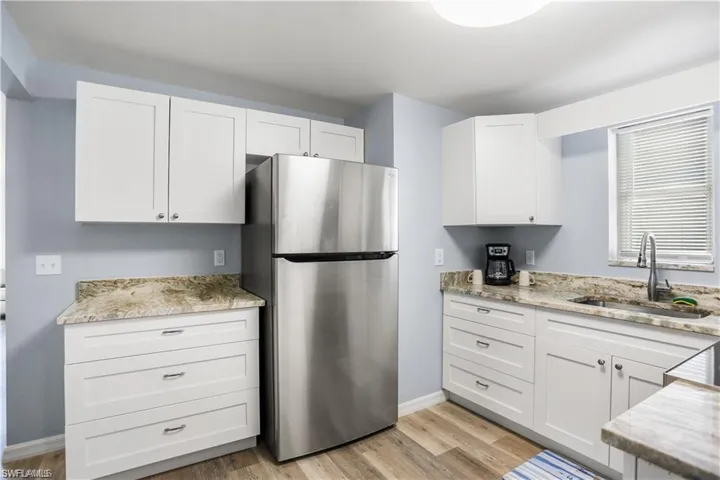 Kitchen with light stone countertops, sink, stainless steel fridge, white cabinets, and light wood-type flooring