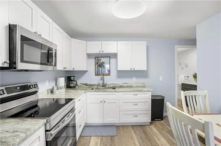 Kitchen featuring white cabinets, sink, light stone countertops, and stainless steel appliances
