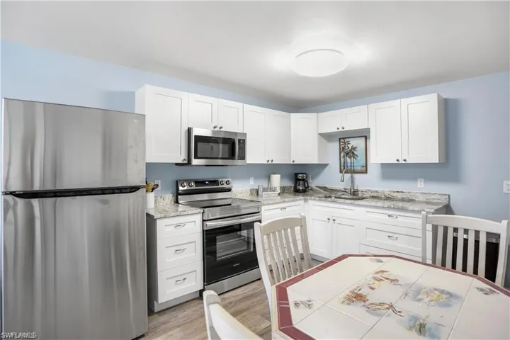 Kitchen with light stone countertops, light wood-type flooring, stainless steel appliances, sink, and white cabinets