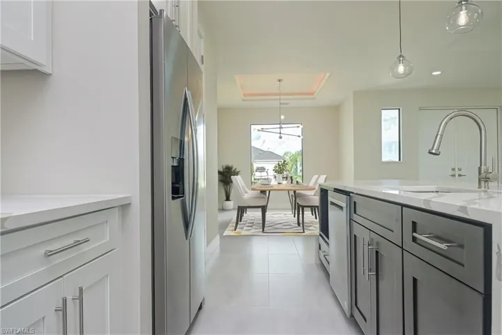 Kitchen with light stone countertops, hanging light fixtures, a tray ceiling, stainless steel appliances, and white cabinetry