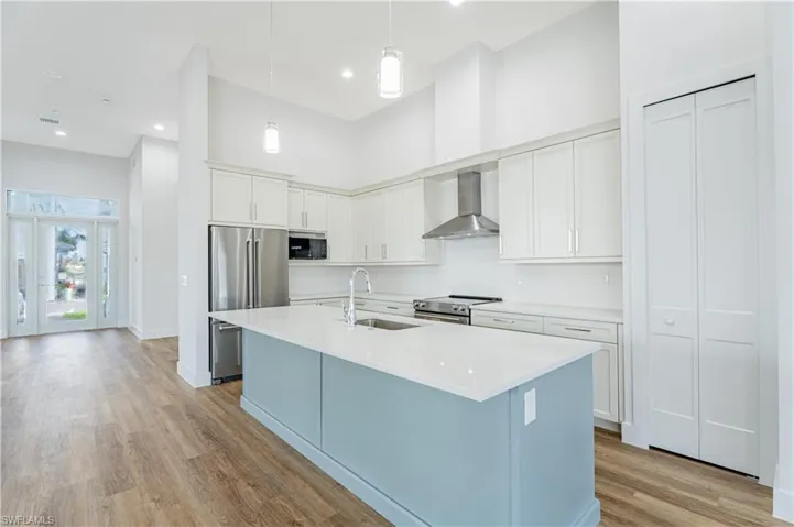Kitchen featuring wall chimney exhaust hood, a kitchen island with sink, stainless steel appliances, sink, and white cabinetry