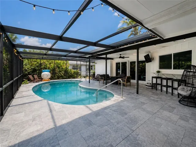 Screened-in outdoor living space with a freeform swimming pool, expansive tile patio, and covered dining area with built-in bar
