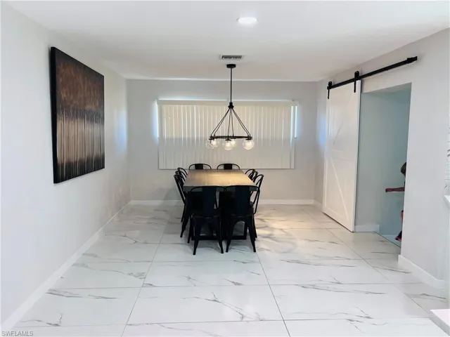 Spacious interior with large format tile flooring, modern linear chandelier, recessed lighting, and a white barn door