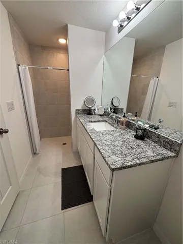 Full bathroom featuring tile patterned flooring, a textured ceiling, tiled shower, and vanity