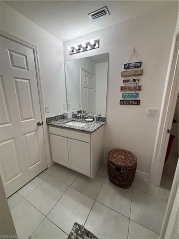 Bathroom with tile patterned floors, visible vents, a textured ceiling, vanity, and a textured wall