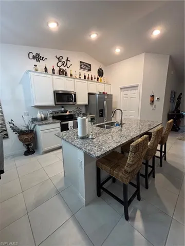 Kitchen featuring stone counters, a kitchen breakfast bar, range, refrigerator, and a sink