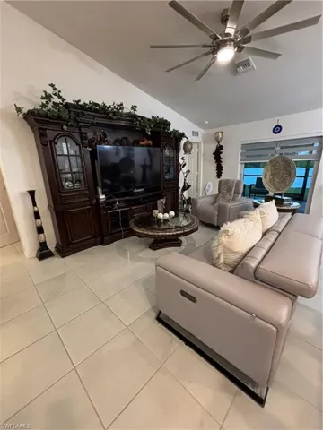 Living room with vaulted ceiling, light tile patterned floors, visible vents, and ceiling fan