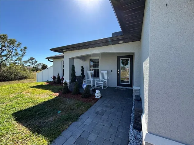 Entrance to property featuring a porch, a lawn, fence, and stucco siding