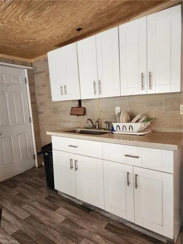 Kitchen with dark hardwood / wood-style flooring, wooden ceiling, white cabinets, sink, and backsplash