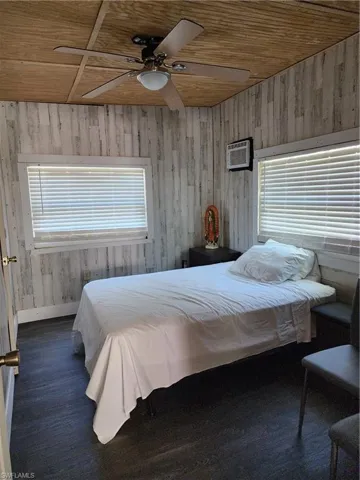 Bedroom featuring wood-type flooring, ceiling fan, wooden walls, an AC wall unit, and wood ceiling