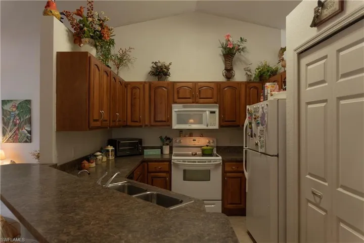 Kitchen featuring lofted ceiling, sink, white appliances, and kitchen peninsula