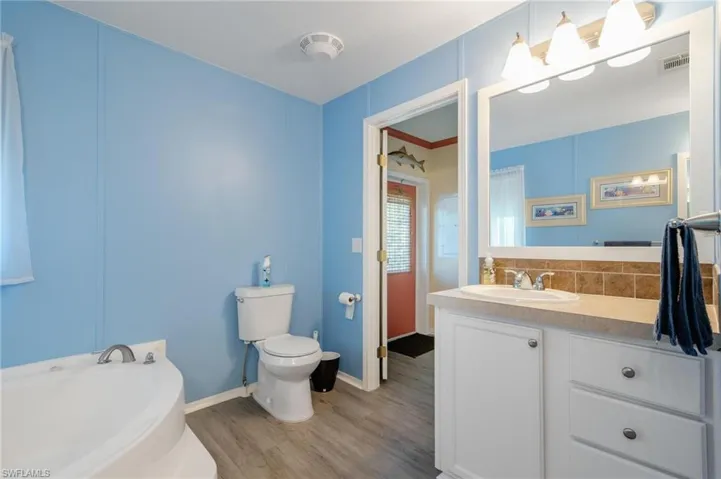 Bathroom with a tub, hardwood / wood-style floors, vanity, tasteful backsplash, and toilet