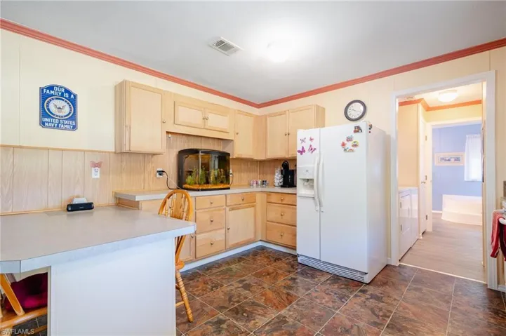 Kitchen with dark hardwood / wood-style flooring, light brown cabinetry, ornamental molding, a breakfast bar, and white fridge with ice dispenser