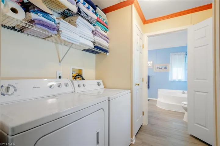 Washroom with light wood-type flooring, ornamental molding, and washer and clothes dryer