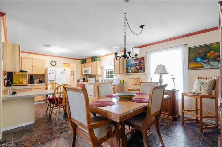Dining area with dark tile patterned flooring, a healthy amount of sunlight, ornamental molding, and a chandelier