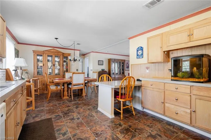 Kitchen with dark tile patterned floors, a kitchen bar, light brown cabinets, and hanging light fixtures