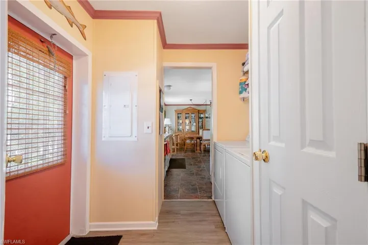 Hallway with ornamental molding, independent washer and dryer, electric panel, and wood-type flooring