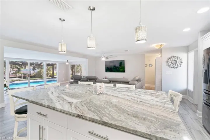 Kitchen featuring a breakfast bar area, white cabinets, light stone counters, pendant lighting, and wood finish floors