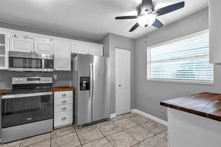 Kitchen with butcher block countertops, stainless steel appliances, a ceiling fan, white cabinetry, and glass fronted cabinets