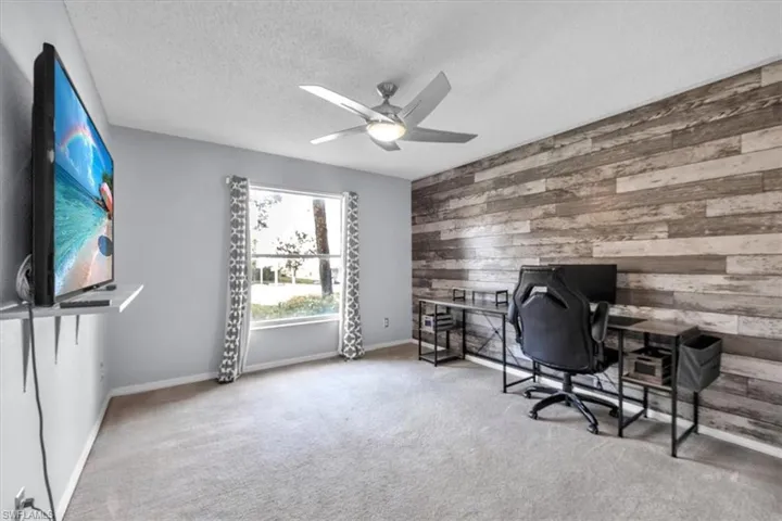 Home office with wooden walls, light colored carpet, a textured ceiling, and a ceiling fan