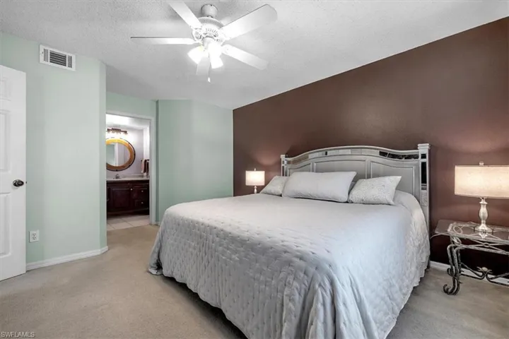 Bedroom featuring light colored carpet, a textured ceiling, ensuite bath, and ceiling fan