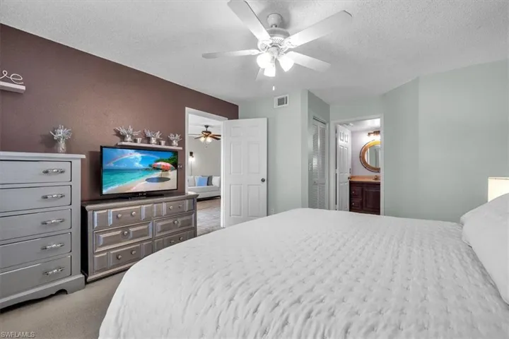 Bedroom with a textured ceiling, light colored carpet, ceiling fan, a closet, and ensuite bathroom
