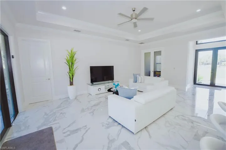 Tiled living room featuring ceiling fan, a tray ceiling, and crown molding
