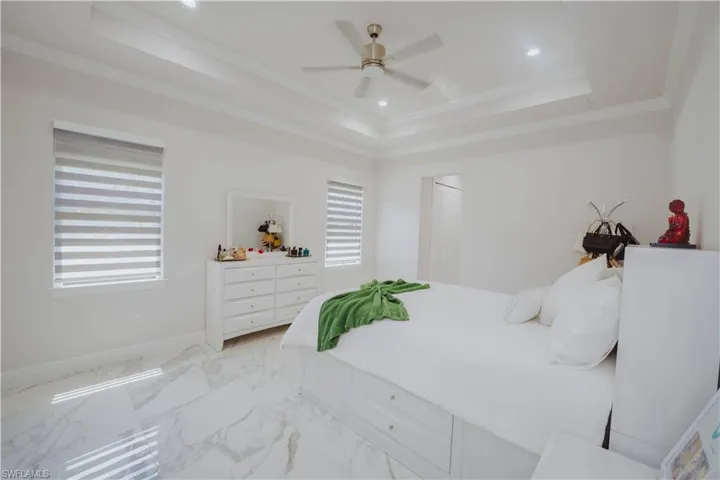 Tiled bedroom featuring crown molding, ceiling fan, a raised ceiling, and multiple windows