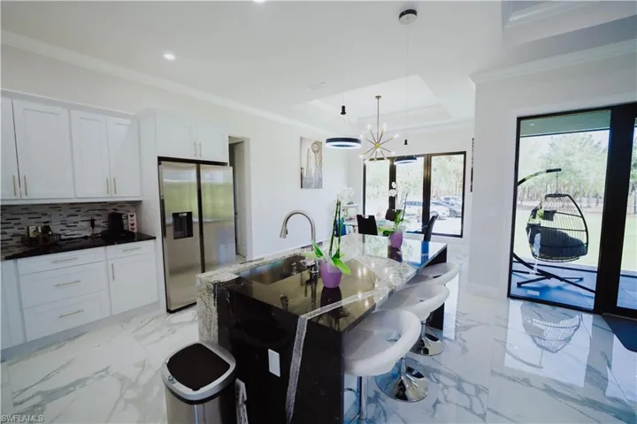 Kitchen with a tray ceiling, backsplash, stainless steel refrigerator with ice dispenser, pendant lighting, and sink