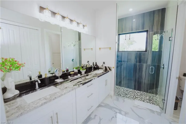Bathroom with tile floors, a shower with shower door, toilet, and dual bowl vanity