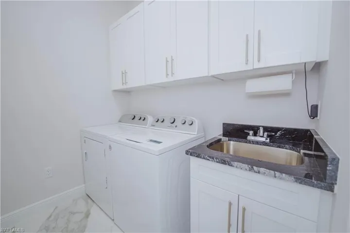 Laundry room featuring cabinets, sink, washer and clothes dryer, and light tile floors
