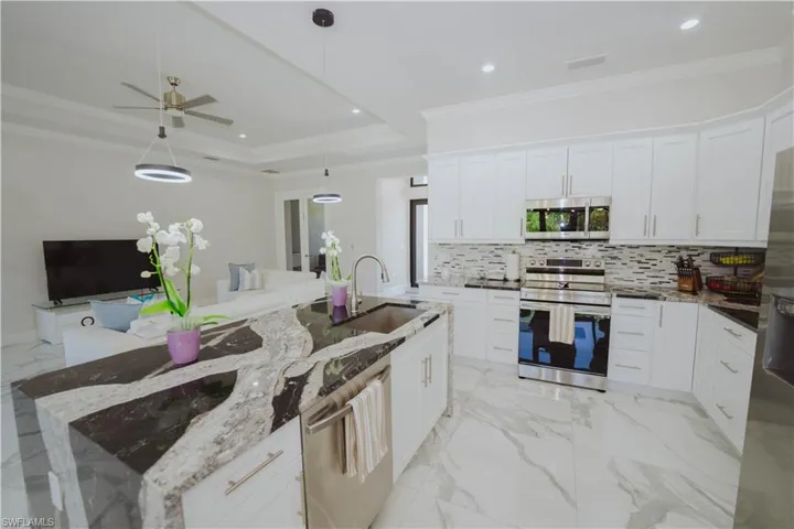 Kitchen with light stone counters, ceiling fan, a tray ceiling, appliances with stainless steel finishes, and sink
