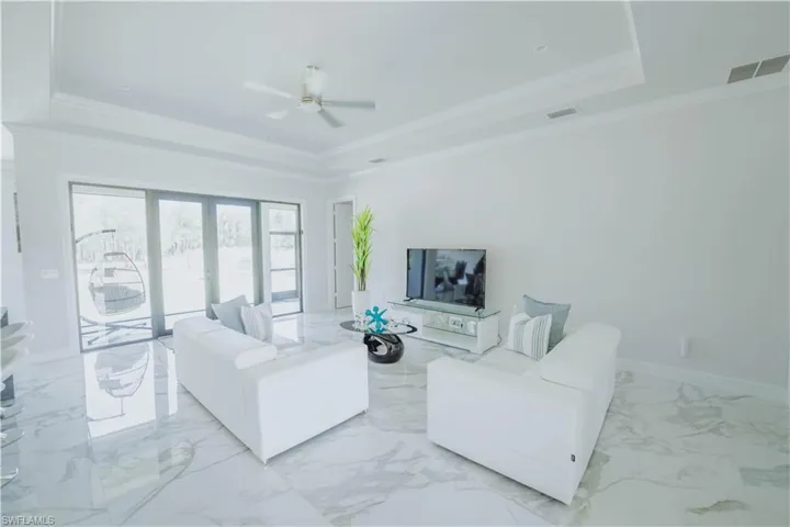 Living room featuring ceiling fan, ornamental molding, a tray ceiling, and light tile floors