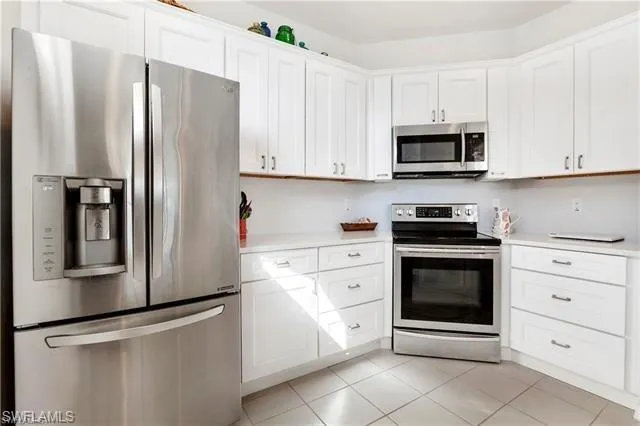 Kitchen with stainless steel appliances, light countertops, light tile patterned flooring, and white cabinetry