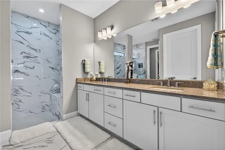 Bathroom with double vanity, a marble finish shower, light marble finish flooring, and recessed lighting