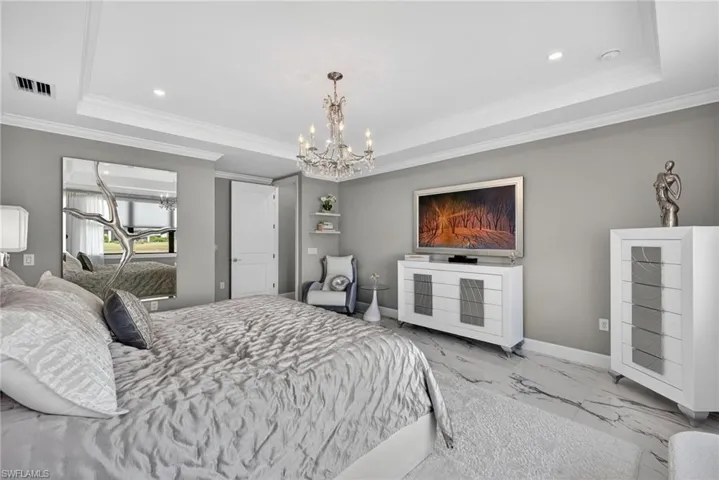 Bedroom with a chandelier, a raised ceiling, marble look tiles, ornamental molding, and recessed lighting