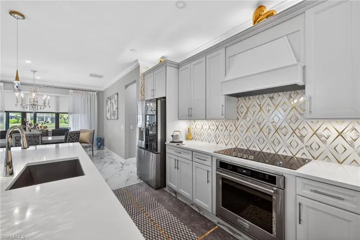 Kitchen featuring stainless steel appliances, crown molding, custom range hood, light stone counters, and pendant lighting