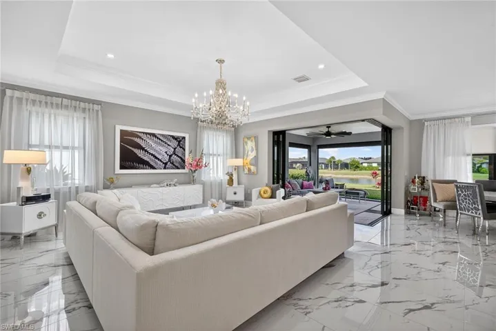 Living room with a chandelier, ceiling fan, crown molding, light marble finish flooring, and a raised ceiling
