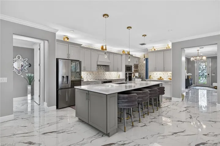 Kitchen with gray cabinets, stainless steel appliances, ornamental molding, a breakfast bar area, and light stone counters