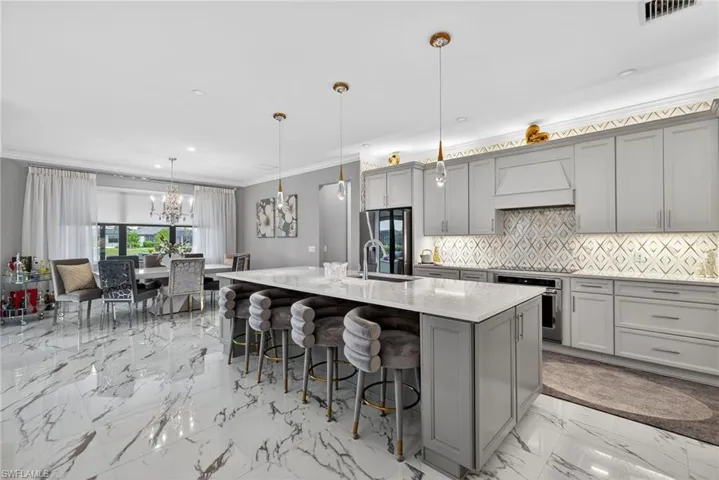 Kitchen featuring ornamental molding, a chandelier, hanging light fixtures, light stone countertops, and a breakfast bar area