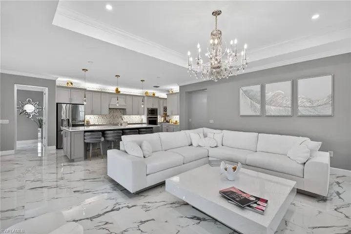 Living area with crown molding, a chandelier, a raised ceiling, and recessed lighting