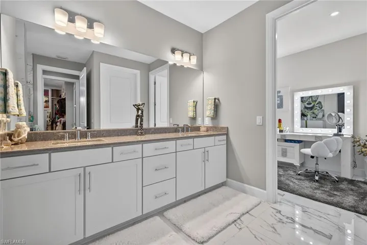 Bathroom with double vanity, light marble finish floors, and a walk in closet