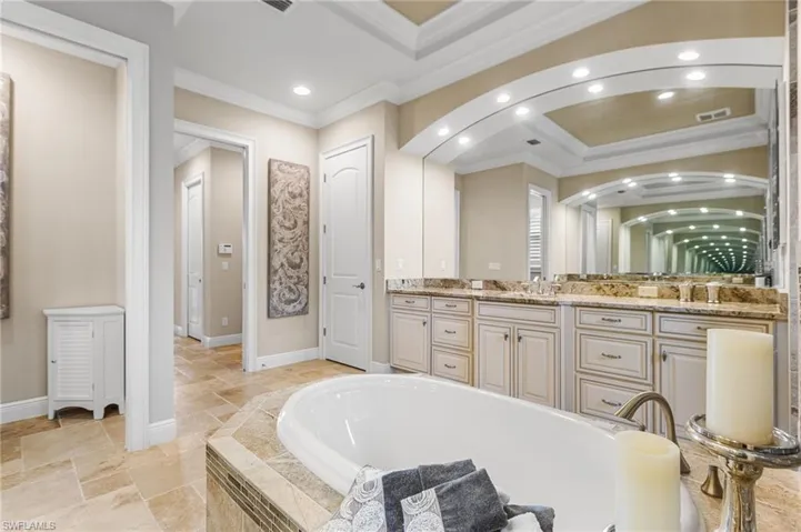 Bathroom featuring ornamental molding, a relaxing tiled tub, vanity, and a tray ceiling